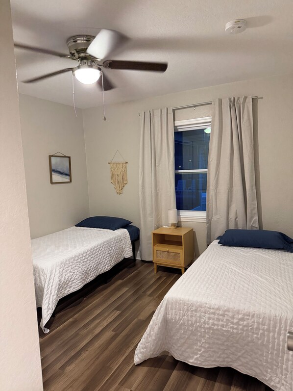 A bedroom with two beds, a ceiling fan, a bedside table with a lamp, a framed picture, and a macrame wall hanging. - Beachy getaway in lovely Lakeland, Fl! (Lakeland)