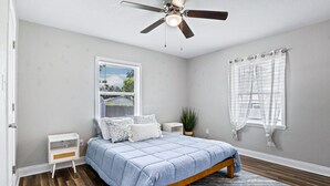 A bedroom with a bed, a ceiling fan, a window with blinds, a nightstand, and a potted plant. - Beachy getaway in lovely Lakeland, Fl!  (Lakeland)