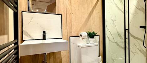 A modern bathroom with a wooden vanity, a white sink, a toilet, and a glass shower enclosure.