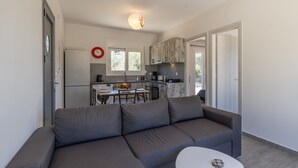 Ein modernes Wohnzimmer mit einem grauen Ecksofa, einem kleinen weißen Tisch und einer Küche im Hintergrund.
