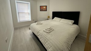Ein Schlafzimmer mit einem großen Bett, weißer Bettwäsche, einem Heizkörper, einem Fenster mit Jalousien und einem Bild an der Wand.