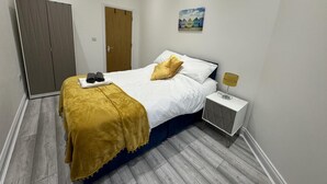 A neatly arranged bedroom with a bed, a bedside table with a lamp, a wardrobe, and a door.