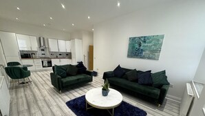 A modern living room with two green sofas, a round coffee table, and a blue rug.