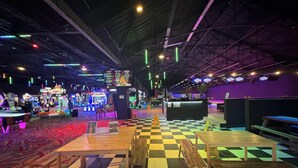 An indoor entertainment venue with arcade games, checkered flooring, and wooden tables and benches.