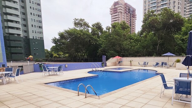 Ein Dachpool mit Liegestühlen und Tischen, umgeben von hohen Wohnhäusern.
