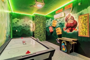 Una habitación con mesa de billar, dardos y un mural que muestra un mono y plátanos.