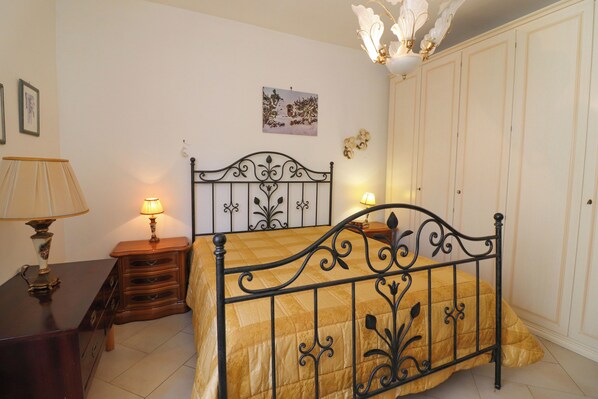 A bedroom with a bed, bedside table, lamp, wall art, and wardrobe.