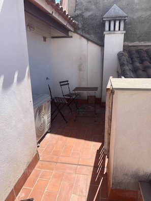 Un petit espace extérieur aménagé en patio, avec une table, des chaises, un ventilateur et un sol carrelé.