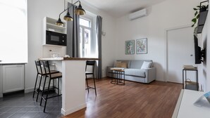 Une cuisine moderne équipée d’un four à micro-ondes, un coin repas avec des chaises, un canapé gris et une petite table.