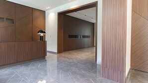 Un espace d’accueil moderne avec un sol en marbre, des panneaux muraux en bois et un bureau agrémenté d’une lampe.