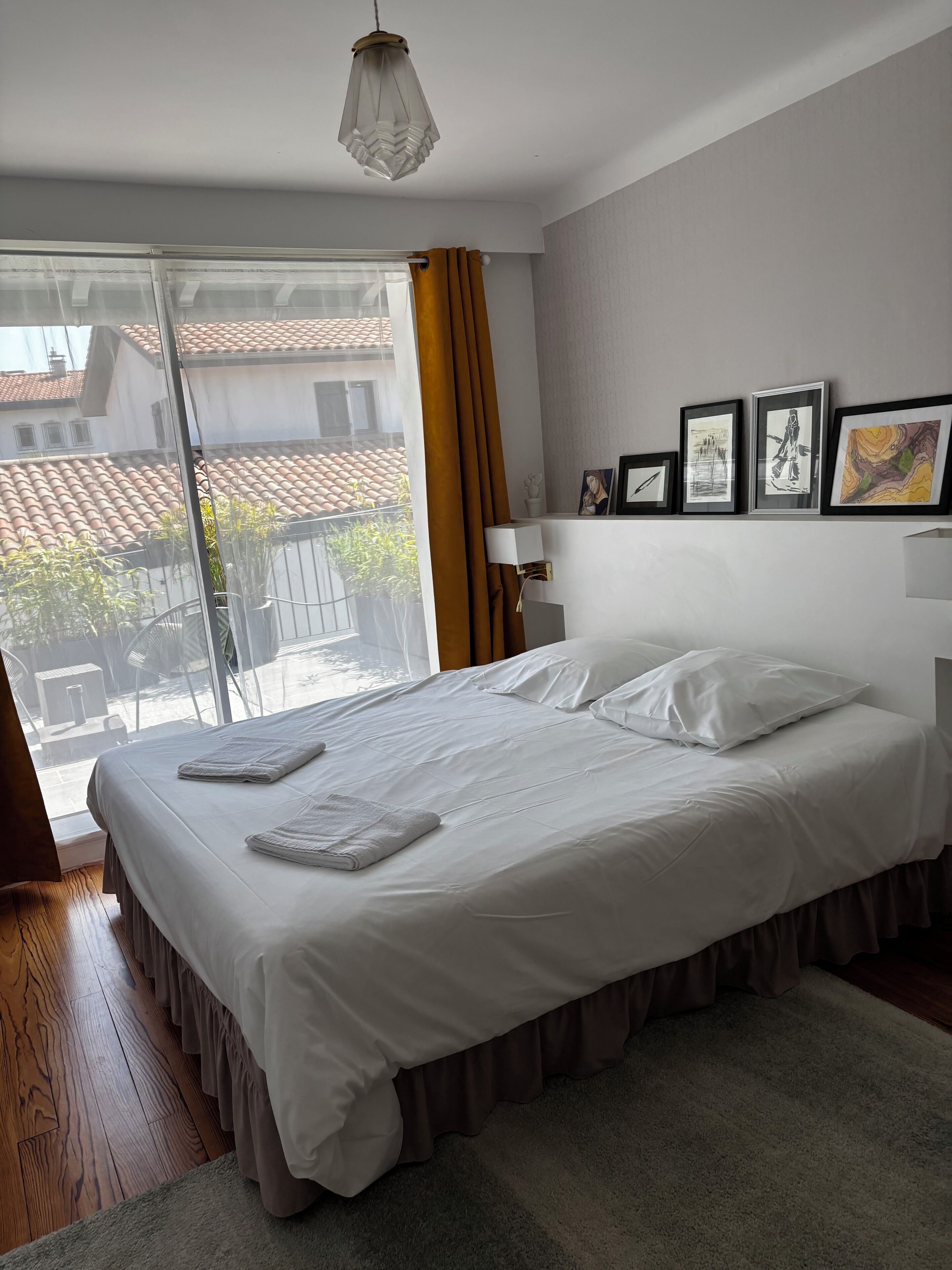 A bedroom with a large bed, a view of the outside, and a wall with framed pictures.