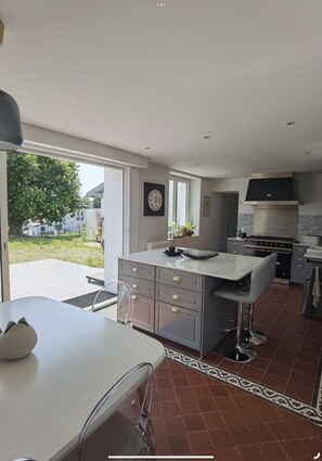 Une cuisine moderne dotée d’un grand îlot central, d’appareils électroménagers intégrés et d’une porte-fenêtre coulissante donnant sur un patio.
