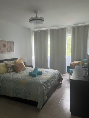 A bedroom with a bed, a desk, a chair, a ceiling light, and a window with curtains. - Beach Condo 3 mins walking distance from the beach, Amazing Pool 2BR Gated Comm. (Punta Cana)