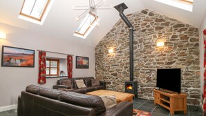 Un salon chaleureux avec un mur en pierre, une cheminée, un canapé en cuir, une table basse en bois et un téléviseur à écran plat.