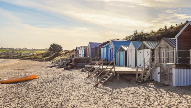 Une rangée de cabanes de plage, avec des escaliers en bois menant à chacune d’elles, située sur une plage de sable.