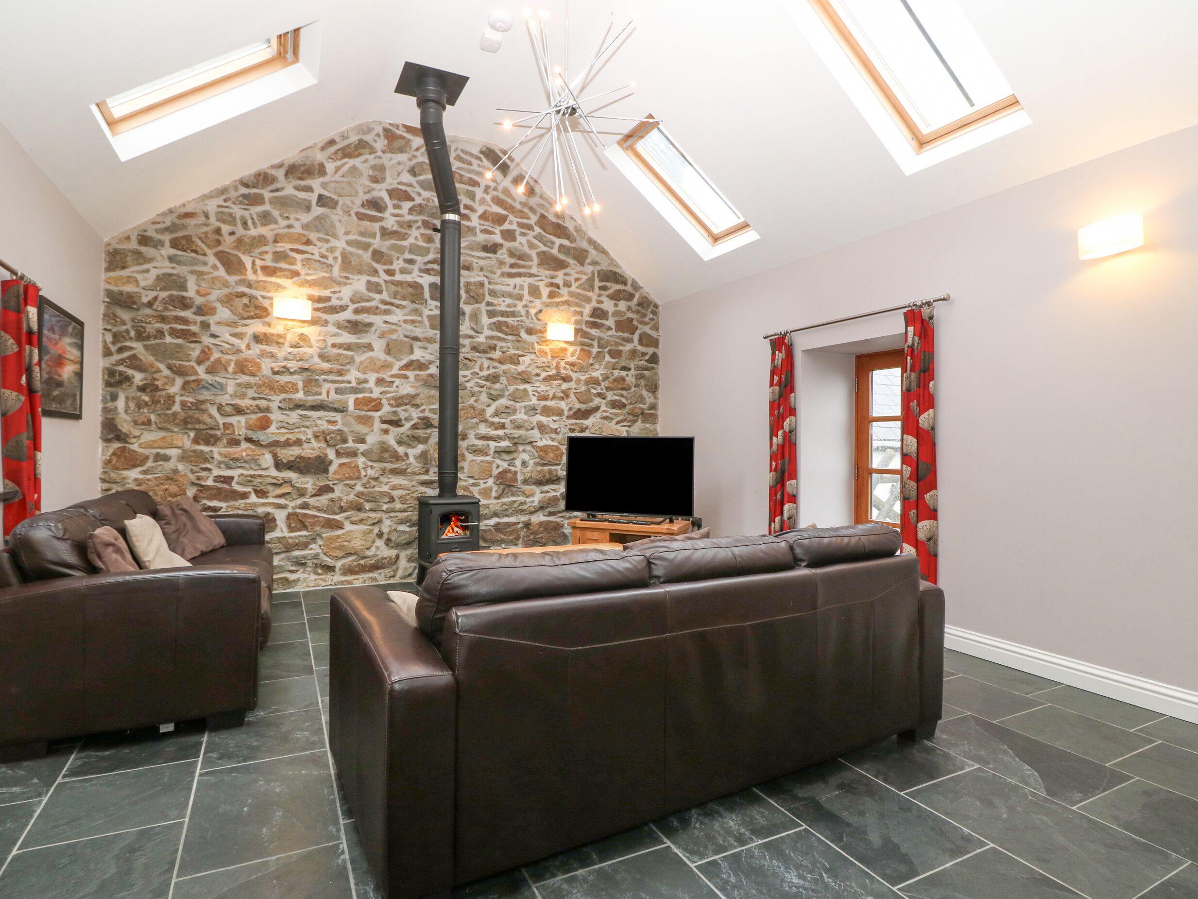 A cozy living room with a stone wall, a fireplace, leather sofas, and a flat-screen TV.