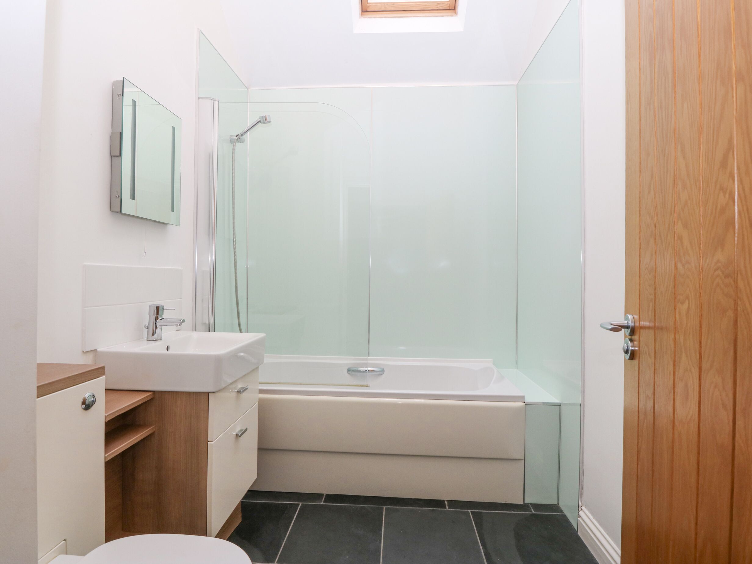 A modern bathroom with a glass shower enclosure, a white bathtub, and a wooden vanity with a mirror.