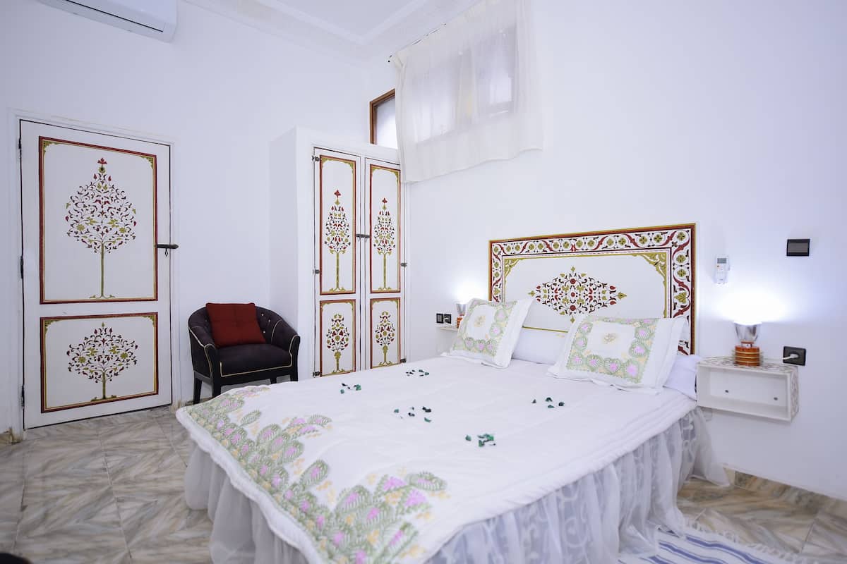 A bedroom with a bed, a chair, a nightstand, and a wall-mounted lamp.
