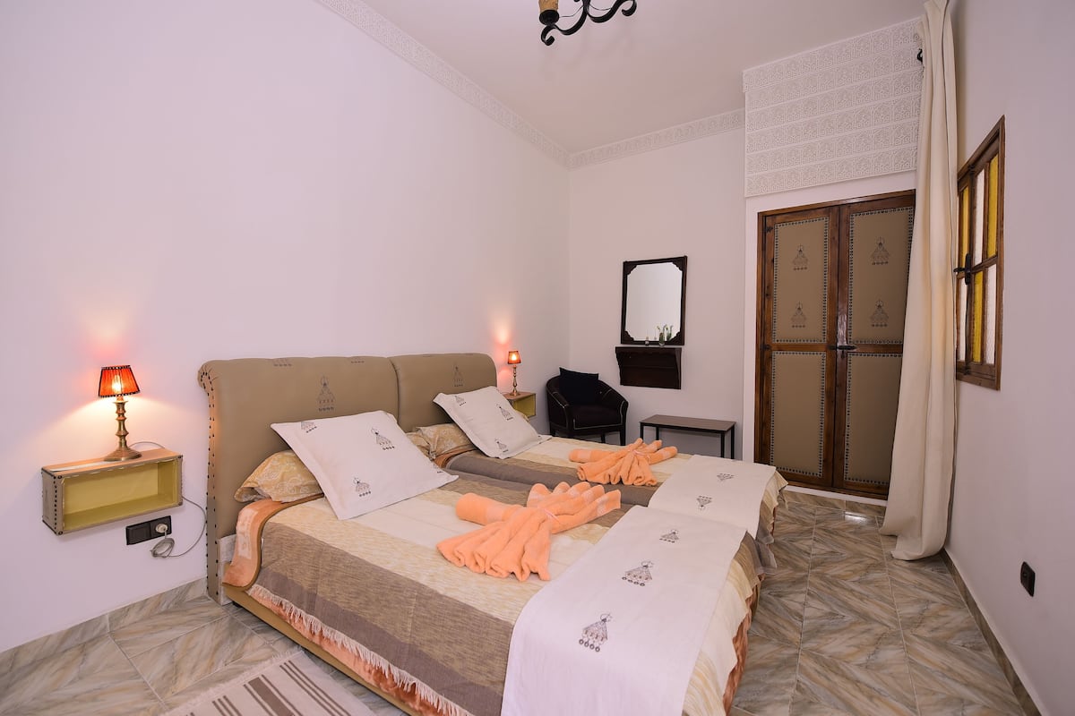 A bedroom with a bed, bedside lamps, a mirror, a wardrobe, and a patterned rug.
