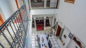A multi-level interior with a dining area featuring a long table, chairs, and a decorative railing. - RYAD RDATE LWALIDINE (Marrakech)