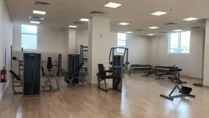 A spacious gym with various exercise equipment, large windows, and a wooden floor.