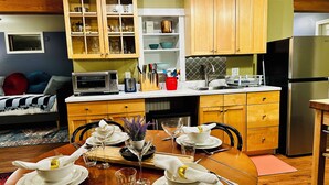 Un coin repas avec une table en bois dressée pour quatre personnes, une cuisine avec des placards en bois, un four à micro-ondes et un réfrigérateur.