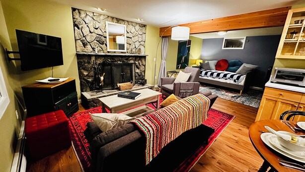 A cozy living room with a fireplace, a sofa, a dining table set for two, and a kitchen area with a microwave.