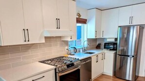 A modern kitchen with white cabinets, stainless steel appliances, and a wooden floor. - Private Garden Suite in Langford - Free car charger (Langford)