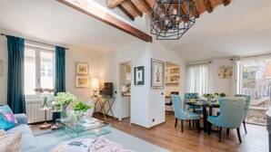 A spacious living area with a sofa, coffee table, and dining table with chairs. There is a kitchen in the background and a balcony with a view. - Clocktower Penthouse (Lucca)
