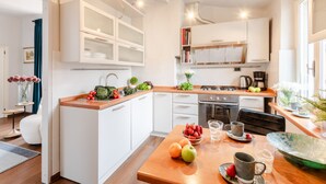 A modern kitchen with white cabinetry, a wooden countertop, and a dining area with a table set for two. - Clocktower Penthouse (Lucca)