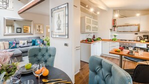 A modern living room with a sofa, a dining table with fruit and glasses, and a kitchen with white cabinets and a wooden countertop. - Clocktower Penthouse (Lucca)