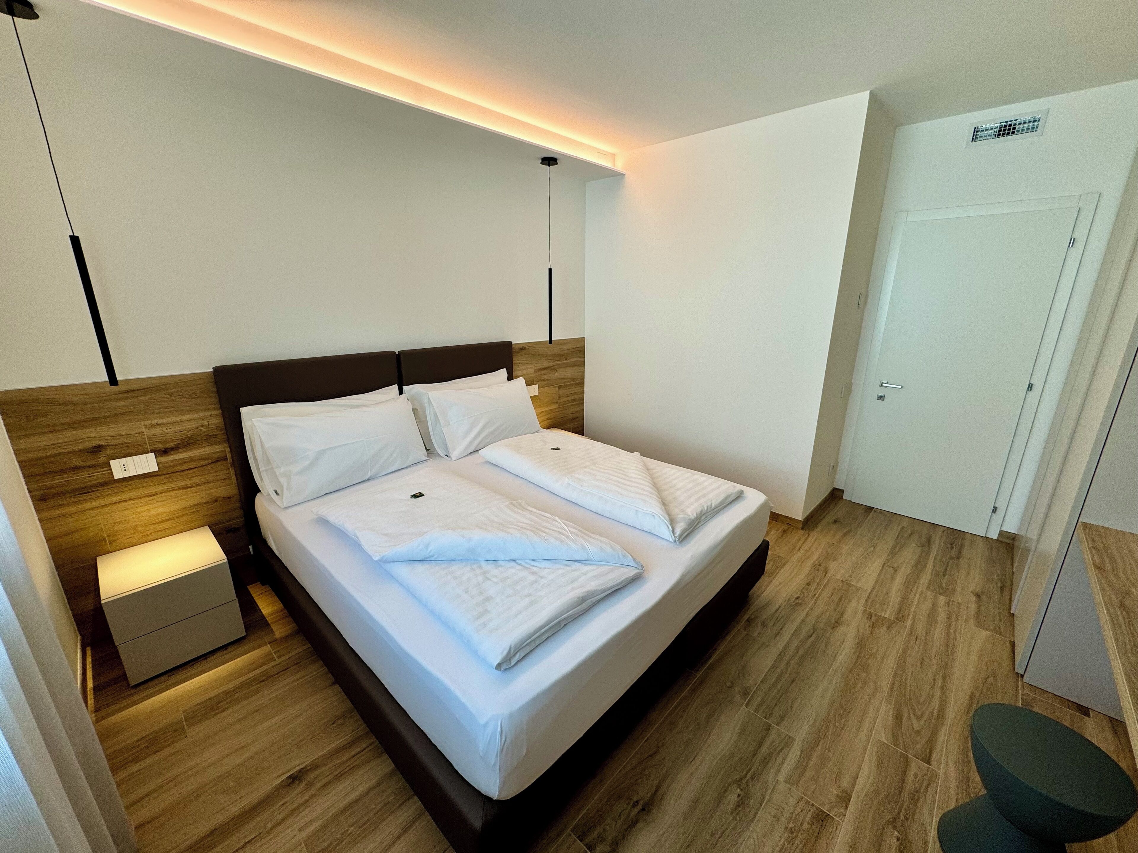 A neatly made bed with white linens, a wooden headboard, and a bedside table with a lamp.