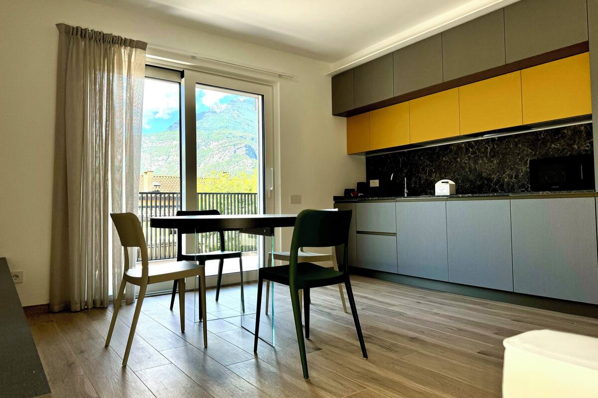 A modern kitchen with grey and yellow cabinets, a black countertop, and a view of mountains through the window.