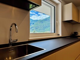 Una cocina moderna con un lavamanos de acero inoxidable, una ventana con vistas a colinas verdes y una cafetera sobre la encimera.