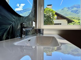 Un baño con un lavamanos moderno, un grifo cromado y una ventana que ofrece vistas a montañas y una casa.