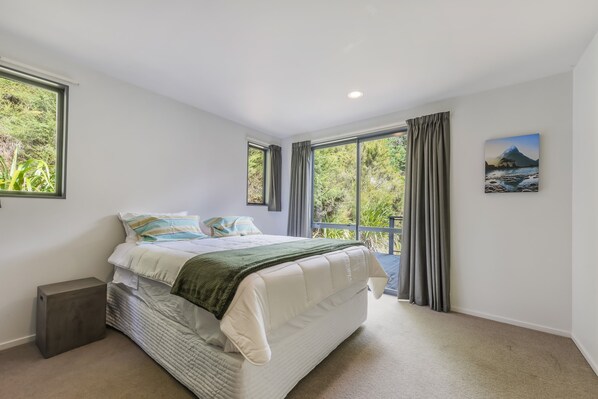 A bedroom with a bed, a nightstand, a window with curtains, and a painting on the wall.