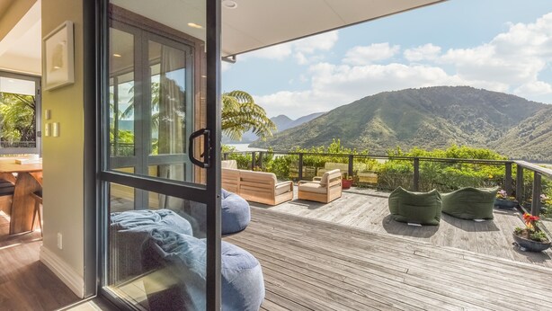 Ein Balkon mit Holzboden, gepolsterten Sitzgelegenheiten und Blick auf Berge.