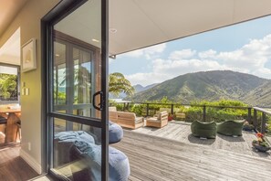 A balcony with wooden flooring, cushioned seating, and a view of mountains. - Tepuia Daze - Havelock Holiday Home (Picton)