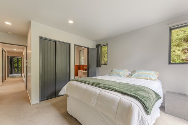 A bedroom with a large bed, a walk-in closet, and a view of greenery outside. - Tepuia Daze - Havelock Holiday Home (Picton)