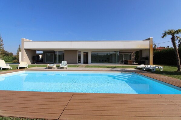 A modern house with a swimming pool, lounge chairs, and a patio area.