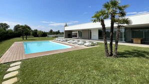 Et moderne hus med swimmingpool, udendørs møbler og palmer.