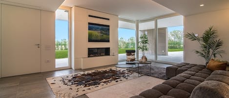 A modern living room with a large sectional sofa, a flat-screen TV mounted on the wall, and a fireplace.