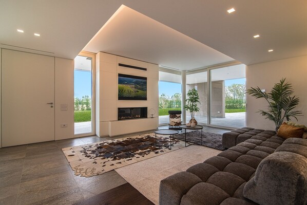 A modern living room with a large sectional sofa, a flat-screen TV mounted on the wall, and a fireplace. - Stima Home With Ac And Pool in Padova (San Gaetano)