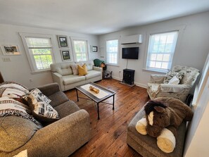 A living room with a sofa, a coffee table, a fireplace, and a television. - Surf & Wind- Fire Pit, Fenced in Yard (Chincoteague)