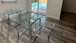 A modern room with a glass-top table and chairs, large windows, and a view of a swimming pool. - Canal Home with Pool near Beaches and Space Center! (Merritt Island)