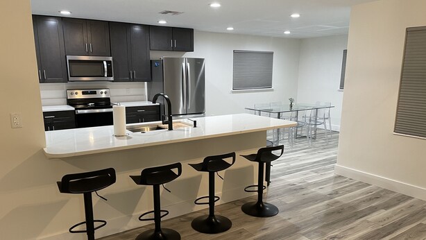 A modern kitchen with dark cabinets, stainless steel appliances, a white countertop, and a bar area with stools. - Canal Home with Pool near Beaches and Space Center! (Merritt Island)