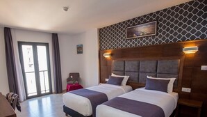 A hotel room with two beds, a large window, a red table, and a patterned wall. - Hotel Santa Cruz Oran (Oran)