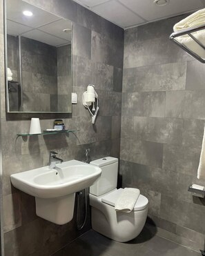 A modern bathroom with a large mirror, a white sink, a toilet, and a towel rack.