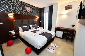 A modern hotel room with a large bed, a desk, and a small refrigerator.