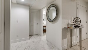 Un couloir aux murs blancs, doté d’un sol en marbre, d’un miroir rond et d’une porte donnant sur une salle de bain.